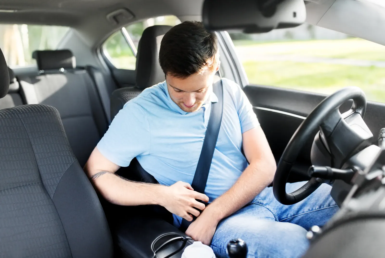 Driver in a passenger car fastening the seat belt across the torso before setting off.