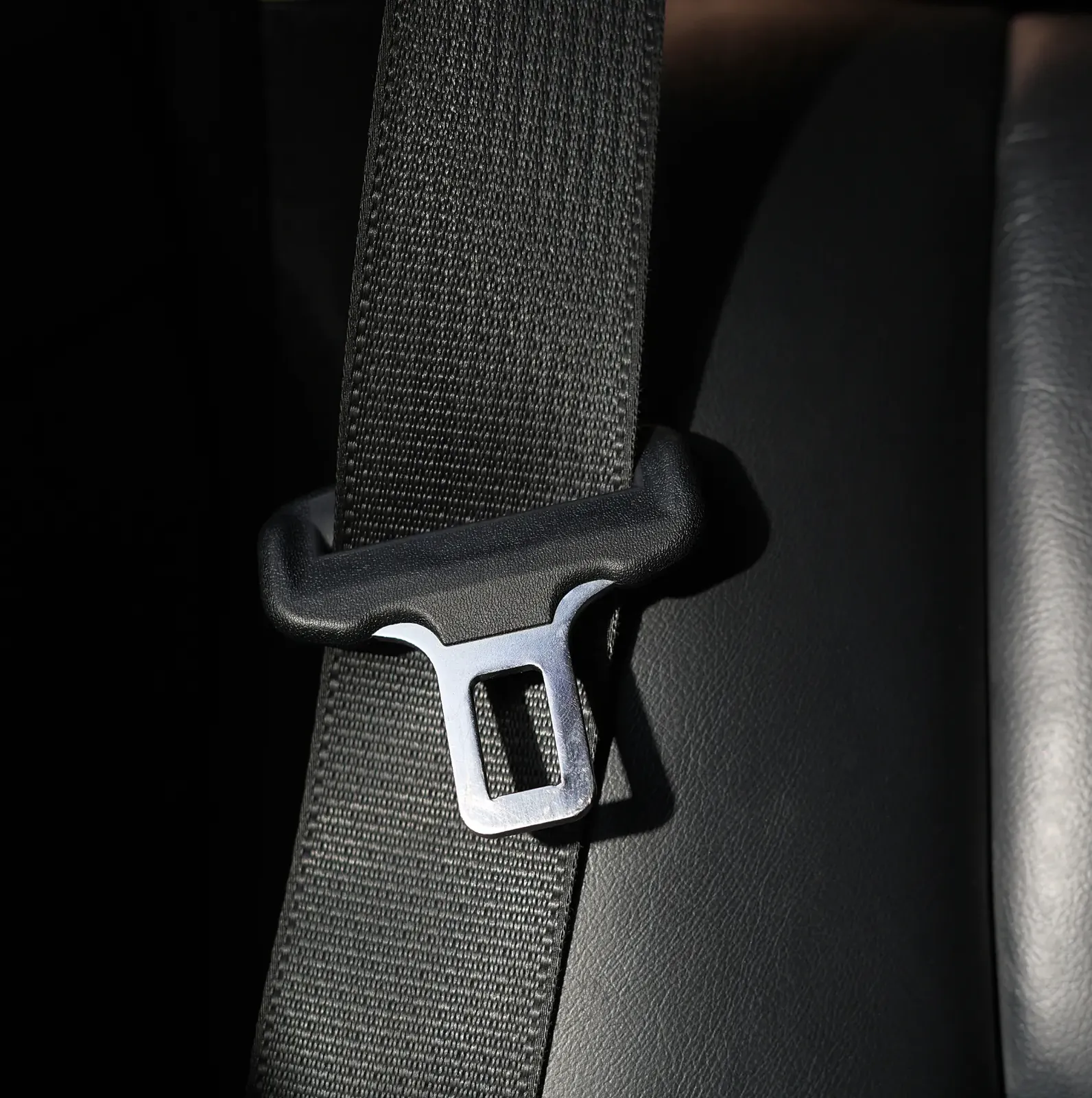Woven black seat belt webbing running into a steel tongue plate seated inside the buckle housing on a dark vehicle seat.