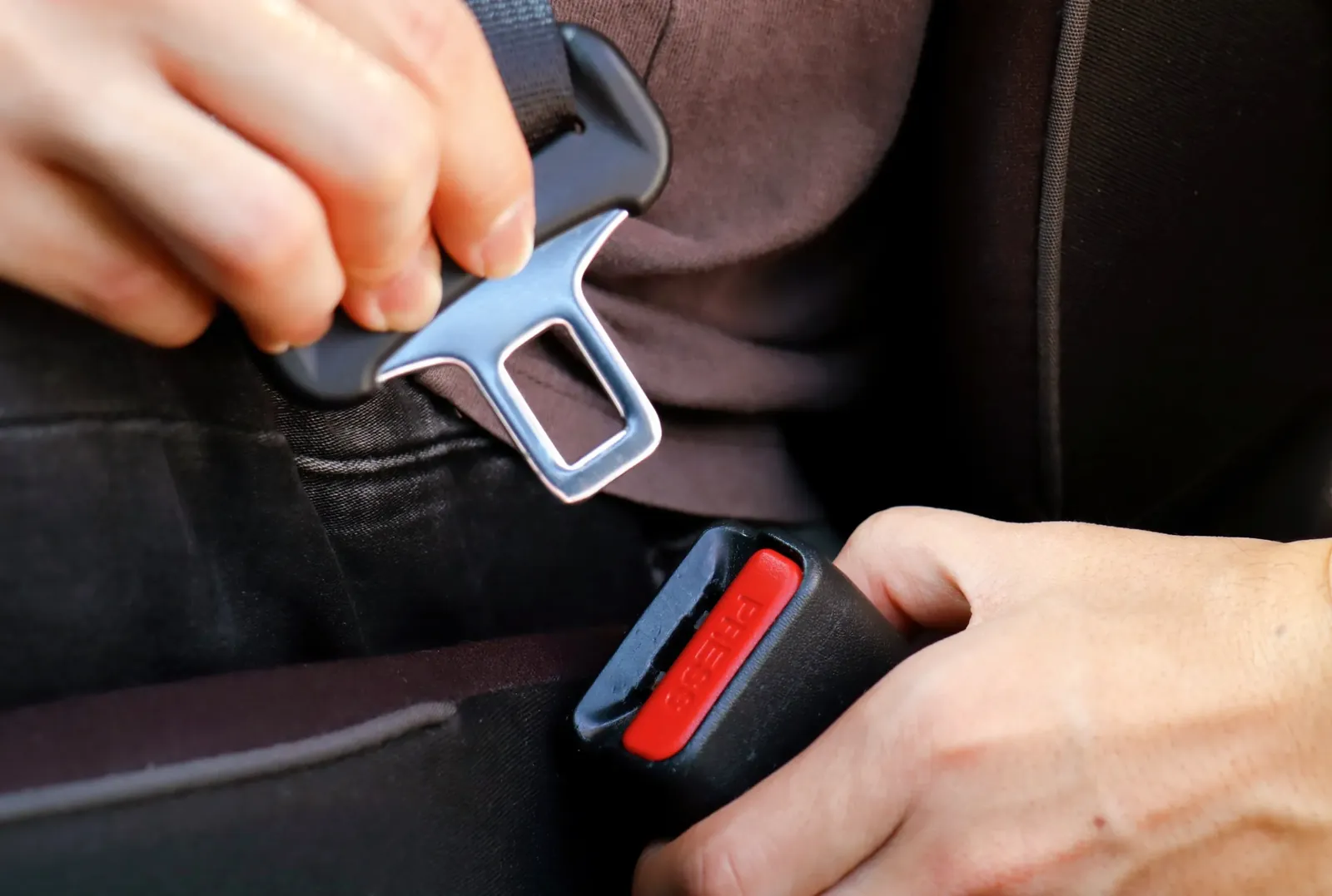 Hands inserting the seat belt tongue plate into the buckle to latch the belt.